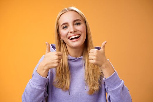 Lifestyle. Close-up charming delighted cute female customer give positive feedback show thumbs-up like gesture smiling broadly agree recommend perfect product skincare standing satisfied orange background.