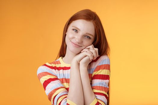 Sweet silly tender redhead young girl leaning palms touched smiling receive charming lovely gift standing thankful look affection sympathy accept dearest romantic gesture, orange background.