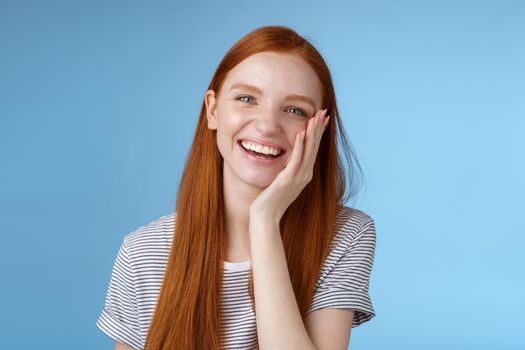 Charismatic talkative friendly-looking happy laughing redhead girl having fun discuss previous summer holidays make jokes chuckling touching face amused standing cheerful blue background.