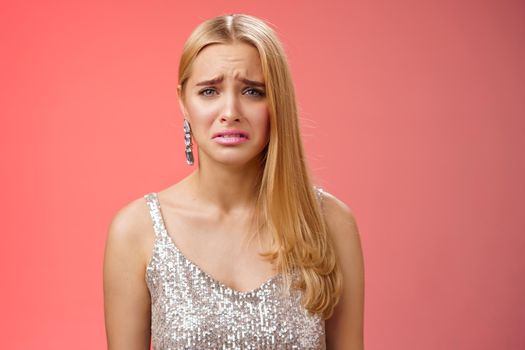 Disappointed complaining cute blond woman in silver stylish dress grimacing frowning upset have bad day pouting pity standing displeased unhappy heartbroken everything bad, red background.