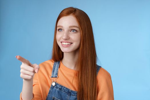 Adorable kind gentle good-looking redhead girl look pointing left amused smiling astonished sighing affection adore stunning breathtaking view glancing mesmerized, blue background.