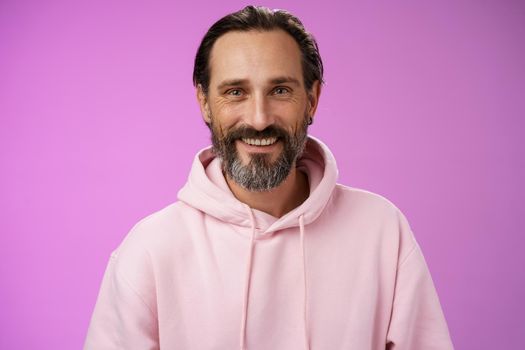 Waist-up happy cheerful caucasian bearded man grey hair in pink trendy hoodie smiling broadly feel healthy attend gym lead active lifestyle grinning white perfect teeth, standing purple background.