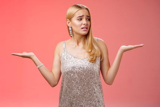 Lifestyle. Anxious insecure young cute blond girl feel lost unsure shrugging hands sideways weighing decisions look right seek help standing lost nervous hesitating red background in silver glittering dress.