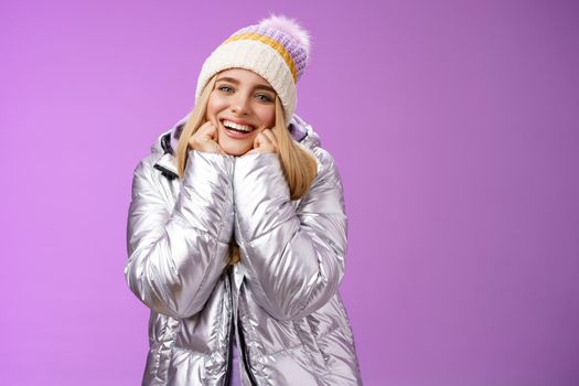 Lifestyle. Delighted charming tender female in stylish cute hat silver shiny jacket lean chin hands smiling sighing enjoying watching lovely romantic scene wanna fall in love standing happily purple background.