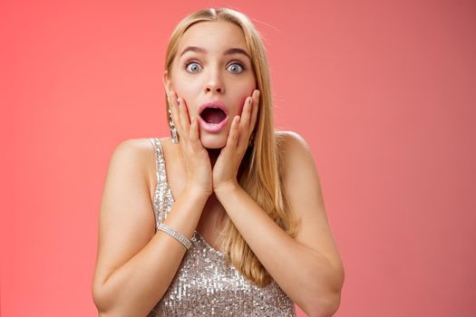 Shocked speechless concerned young stunned woman gasping screaming worried drop jaw touch cheeks widen eyes surprised nervously staring camera troubled afraid, standing red background.