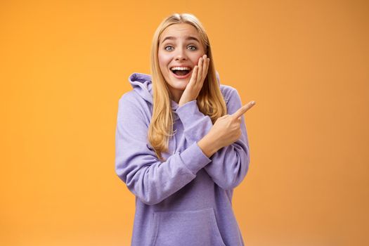 Lifestyle. Amused excited speechless happy young blond woman 25s in hoodie cannot believe luck happiness pointing right amazed smiling broadly touch cheek surprised receive awesome unexpected gift.