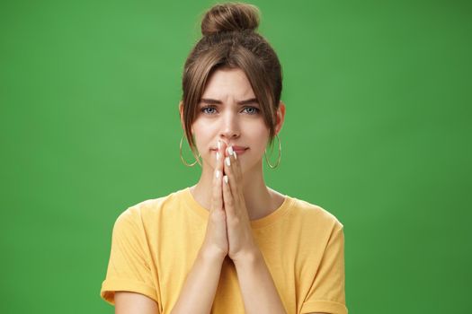 Waist-up shot of nervous upset girlfriend holding hands in pray over lips frowning looking concerned worrying for boyfriend standing anxious and sad over green background. Emotions and body language concept