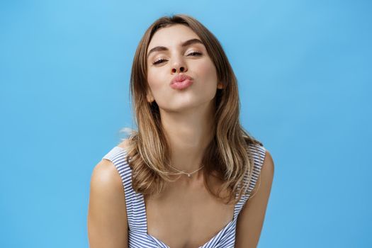 Self-assured happy and charismatic young sensual girlfriend pulling face towards camera, folding lips to give passionate kiss standing delighted and confident in own skin, making photo to post online.