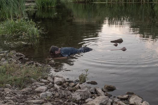 the body of a man who drowned lies face down in the water, the lifeless body of a murdered young man on the river.artistic photo painting, selective focus ,