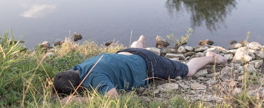 a lifeless dead body lies on the shore of a lake, a young man killed by water. artistic photo painting, selective focus ,