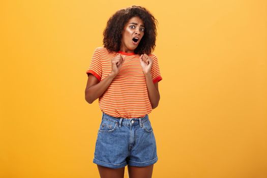 No do not hurt me. Scared silly and insecure good-looking african american woman in stupor screaming for help turning away raising palms near body in defence standing in fright over orange wall. Copy space