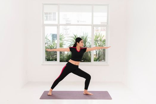 Young attractive woman practicing yoga, standing in Warrior two exercise, wearing sportswear, indoor full length near window