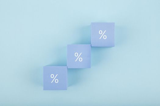 Toy blocks as a ladder with percentage sign on bright pastel blue background. Modern concept of inflation, percent, mortgage or interest rate growth or increase