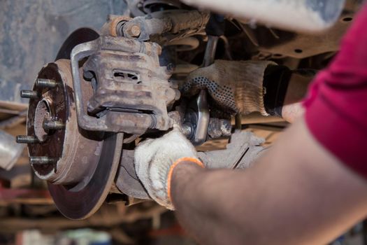 Close-up male hands install or remove the caliper on the wheel of an old car. In the garage, a man changes parts on a vehicle. Small business concept, car repair and maintenance service. UHD 4K.