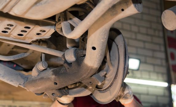 Rusty lower longitudinal and transverse rear rods on an old car. In the garage, a man changes parts on a vehicle. Small business concept, car repair and maintenance service. UHD 4K.