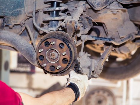 A gloved hand blows compressed air over the rear brake pads on a rusty hub. In the garage, a man changes parts on a vehicle. Small business concept, car repair and maintenance service. UHD 4K.