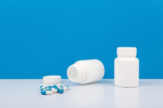 Creative composition with two white medication bottles with pills against blue background with copy space. Concept of healthcare and medical treatment