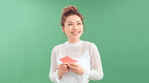 surprised asian young woman holding greeting card while standing isolated on green