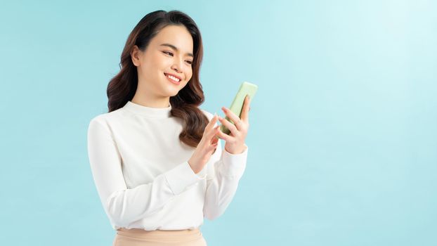 Modern lifestyle and communication. Smiling beautiful girl talking on phone while standing on blue background 