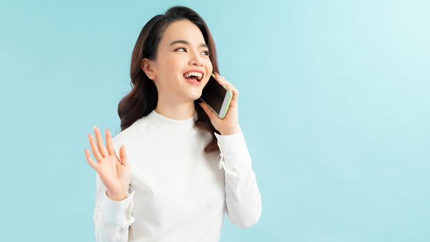 Modern lifestyle and communication. Smiling beautiful girl talking on phone while standing on blue background 