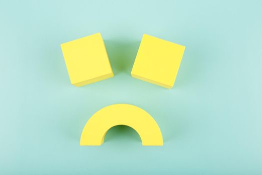 Creative flat lay with unhappy, sad smile symbol made of yellow figures on blue background. Concept of emotions, emoji, mental health or unsatisfied customer or bad service