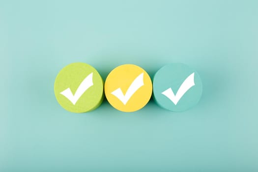Three white checkmarks on multicolored toy circles in a row in the middle on bright aqua blue background. Concept of questionary, checklist, to do list, planning, business or verification.