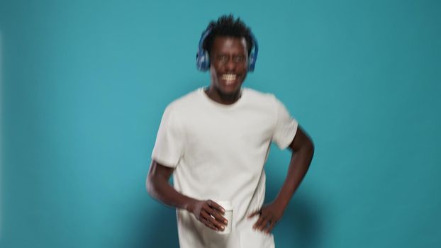 Portrait of man with headphones jumping and dancing to song. Playful person listening to music on headset while doing funny moves on song audio. Adult having fun with rhythm and sound