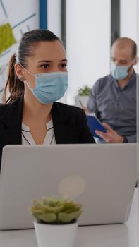 Business team with medical face masks working together in startup company office during coronavirus global epidemic. Team checking business reports while keeping social distancing