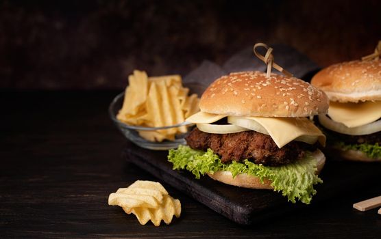 A set of homemade delicious burgers of beef, onion, cheese and lettuce on a dark wooden background. Fat unhealthy food close-up. With copy space.