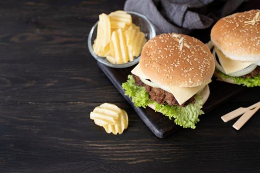 A set of homemade delicious burgers of beef, onion, cheese and lettuce on a dark wooden background. Fat unhealthy food close-up. With copy space.