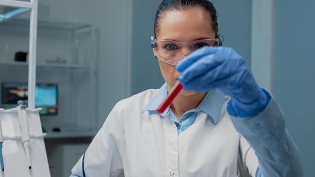 Chemistry specialist looking at sample of blood from vacutainer in laboratory. Doctor woman holding glass flask with fluid for examination. Chemical tubes in microbiology lab industry
