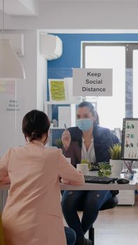 Business womens with medical face masks talking about management statistics working at desk table in new normal company office. Team mantain social distancing to avoid infection with coronavirus