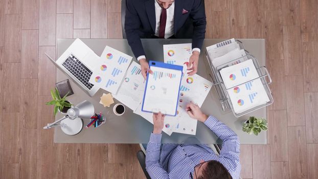 Top view of businessmen sharing company documents analyzing financial profit during business collaboration in startup office. Entrepreneurs discussing management investments. Corporate presentation