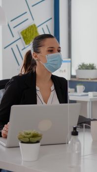 Business team looking at financial strategy in office company wearing face mask to prevent infection with covid19 while keeping social distancing. Coworkers typing on computer for marketing project