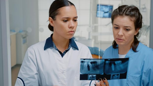 Dentistry nurse and stomatologist examining dentition scan at dental clinic for professional teeth care consultation. Orthodontic staff looking at radiography for patient operation