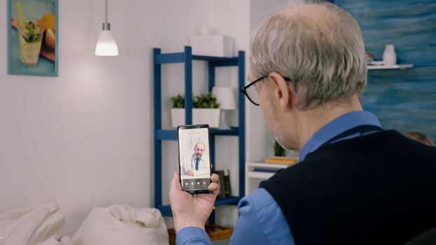 Senior business man discussing during video conference with remote doctor holding smartphone. Young physician explaning medical treatment on videocall using modern technology network wireless