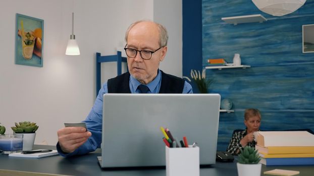 Retired man making shopping online doing payment using credit card on laptop working from home. Senior person paying bills, making ecommerce transactions using modern technology via internet