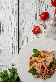 conchiglioni pasta with cherry tomatoes, cheese and parsley in white plate on wooden background, top view copy space