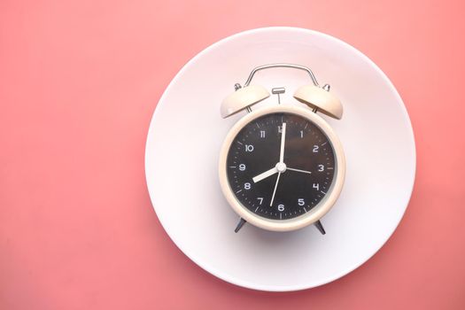 Alarm clock on plate on on a pick background .