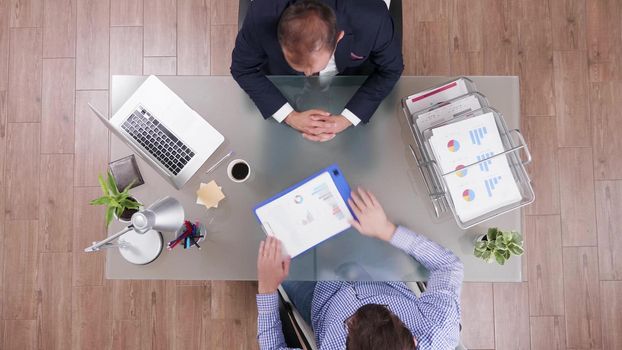 Top view of businessman analyzing financial documents discussing company strategy with partner during partnership meeting in startup office. Colleagues planning business strategy. Corporate agreement