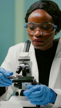 Portrait of pharmaceutical woman putting slide under microscope examining biological sample for medical experiment. Biologist analyzing organic agriculture plants in microbiology scientific laboratory