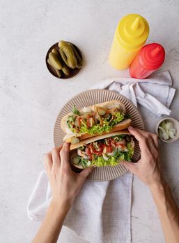 Hot dog with sausage, letuce, cucumber and onion on beigw plate on wooden background. Top view. Flat lay.