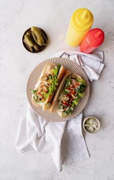 Hot dog with sausage, letuce, cucumber and onion on beigw plate on wooden background. Top view. Flat lay.