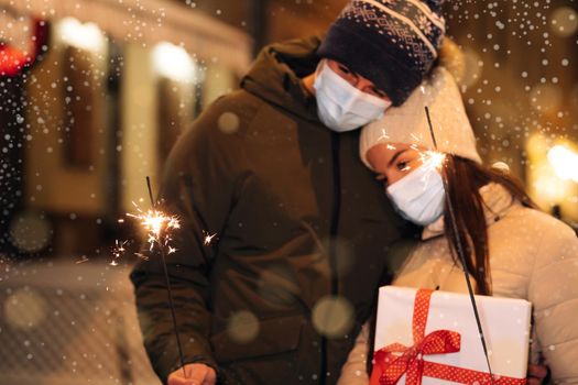 Unrecognizable Couple Hands holding and waving sparklers. Party on occasion of New Year, Christmas Eve or Xmas. Lifestyle. Couple in protective medical masks standing on the street holding sparklers.