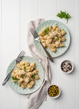 radiatori pasta with cherry tomatoes, cheese and parsley in white plate on wooden background, top view copy space