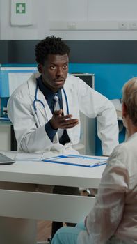 Nurse giving doctor x ray result for patient consultation in medical office at healthcare clinic. Young medic holding radiography, explaining diagnosis and disease to senior woman