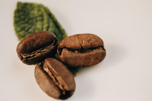 Three shiny fresh roasted coffee beans with leaves isolated on white background