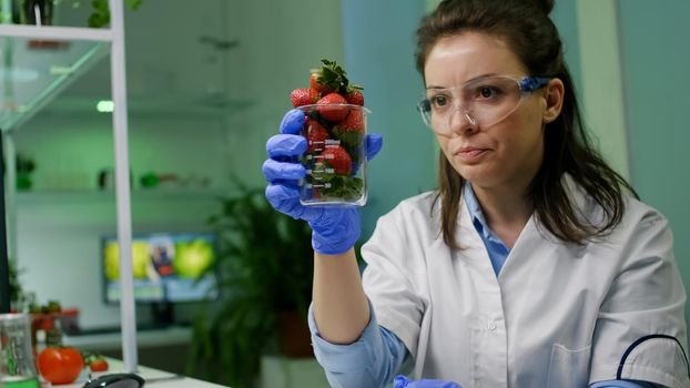 Chemist typing medical botany expertise on computer for agriculture experiment analyzing glass with organic strawberry researching for genetic mutation. Botanist researcher working in farming lab