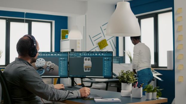 Mecanic technician working on cad software using computer with two monitors innovating an efficient eco-friendly motor prototype. Industrial man engineer studying new idea in creative office