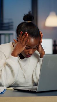 Stressed african businesswoman suffering from headache at work doing overtime late night. Exhausted tensed worker coping with migraine, emotional stress concept feeling pain working at laptop